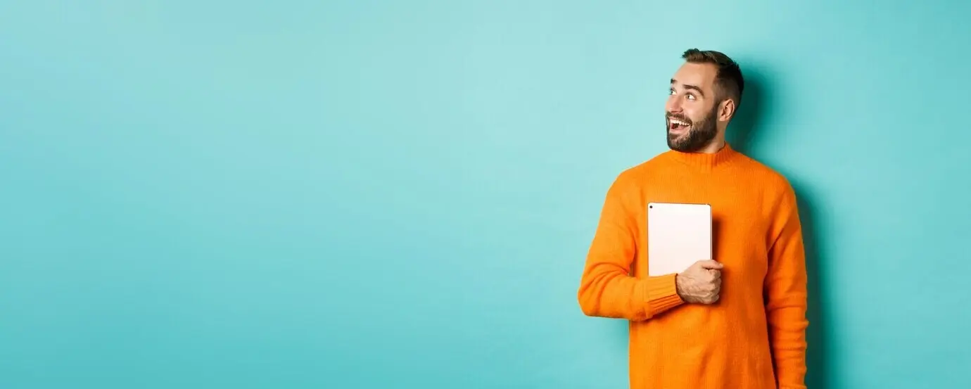 Gutaussehender Mann hält einen Laptop, blickt überrascht und erstaunt nach links und steht in einem orangefarbenen Pullover.